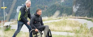 Mann schiebt Rollstuhlfahrer auf einem barrierefreien Wanderweg