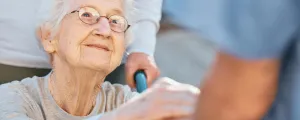 Frau im Rollstuhl gibt Pflegerin die  Hand