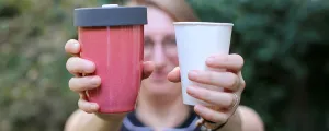 Frau zeigt Plastikbecher und wieder verwertbaren Becher