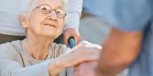 Frau im Rollstuhl gibt Pflegerin die  Hand