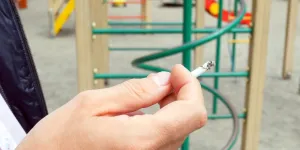 Mann auf Spielplatz hält eine Zigarette