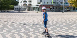 Mädchen skatet auf einem Skateboard auf einem Platz vor einem Hochhaus