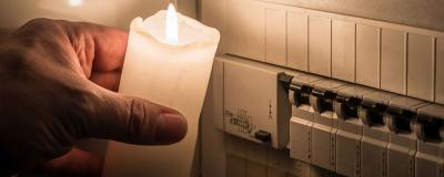 Sicherungskasten mit Sicherungen in einem Verteilerkasten während eines Stromausfall mit weißer Kerze beleuchtet die ein Mann in der Hand häl