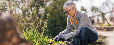 Eine ältere Frau mit kurzen Haaren arbeitet im naturnah gestalteten Garten.
