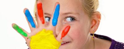 Kind mit Fingerfarben lacht in die Kamera