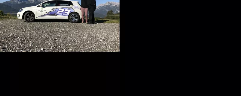 Paar steht mit Auto vor Bergkulisse