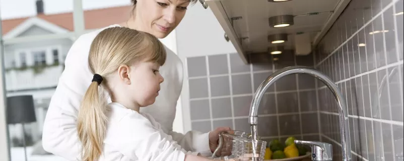 Mutter und Tochter trinken von der Wasserleitung