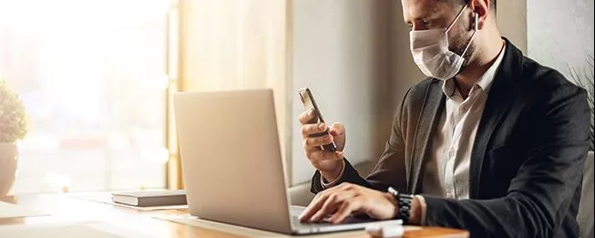 Mann sitzt mit Maske vor Laptop