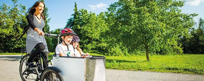 Frau mit Lastenfahrrade in dem sie ein Kind transportiert.