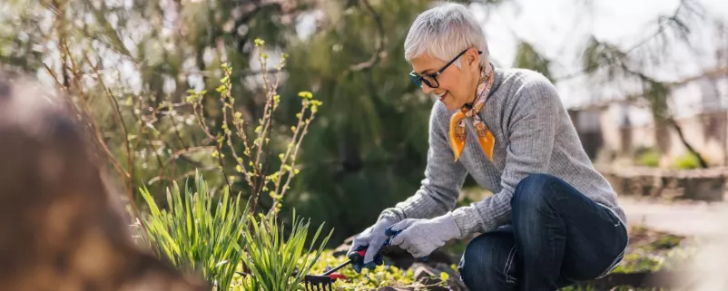 Eine ältere Frau mit kurzen Haaren arbeitet im naturnah gestalteten Garten.