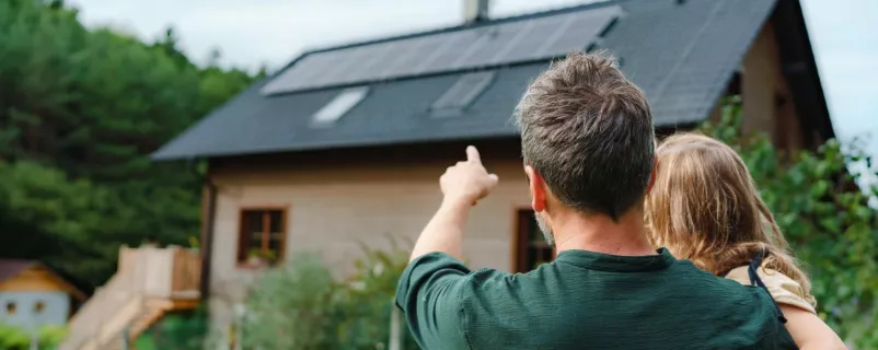 mann mit Kind deutet auf Haus mit PV-Anlage