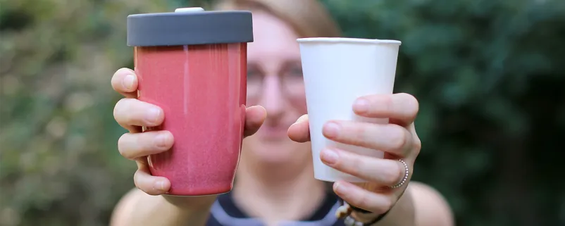 Frau zeigt Plastikbecher und wieder verwertbaren Becher