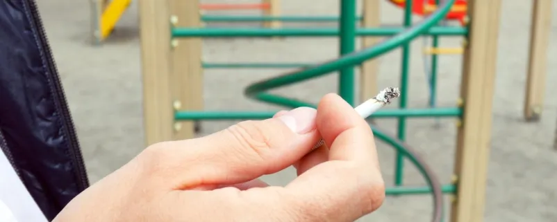 Mann auf Spielplatz hält eine Zigarette