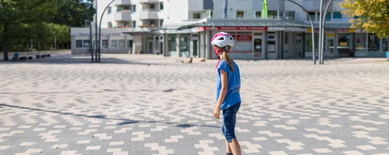 Mädchen skatet auf einem Skateboard auf einem Platz vor einem Hochhaus