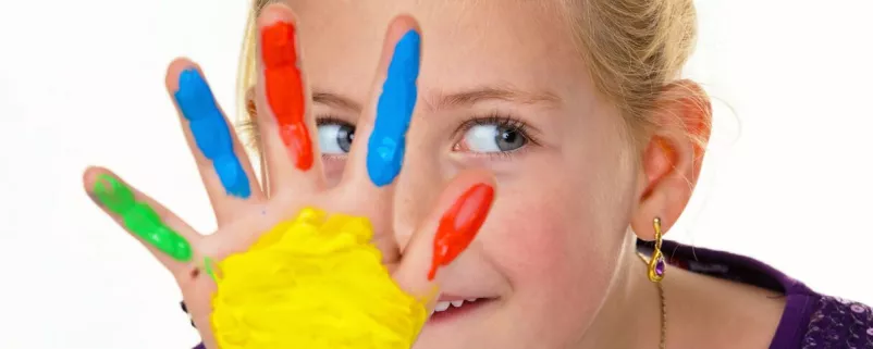 Kind mit Fingerfarben lacht in die Kamera