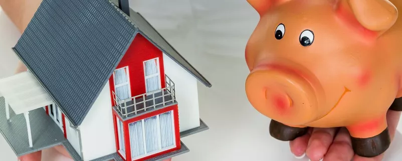 Ein Sparschwein neben einem Spielzeug-Haus