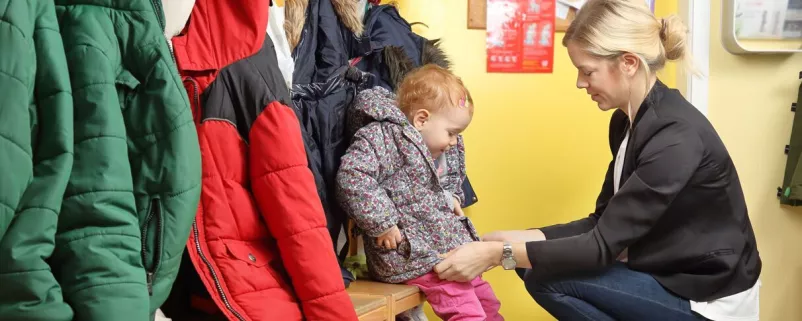 Mutter zieht Kind in der Garderobe an