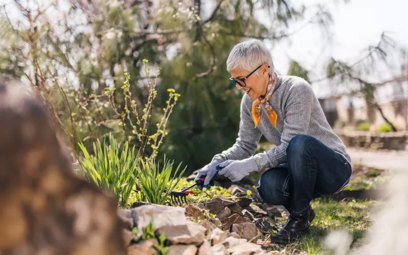 Eine ältere Frau mit kurzen Haaren arbeitet im naturnah gestalteten Garten.