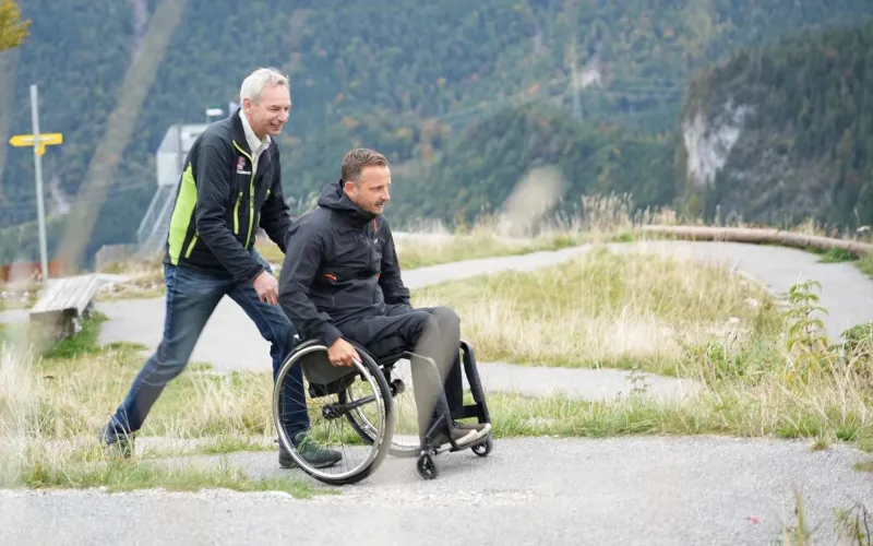 Mann schiebt Rollstuhlfahrer auf einem barrierefreien Wanderweg