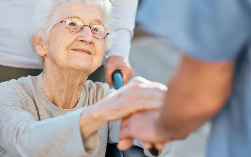 Frau im Rollstuhl gibt Pflegerin die  Hand