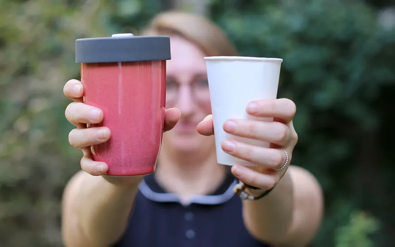 Frau zeigt Plastikbecher und wieder verwertbaren Becher