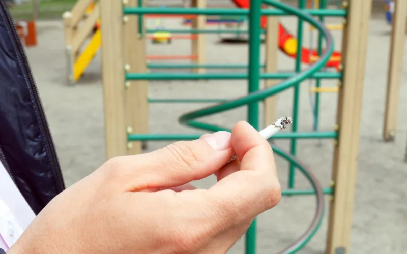 Mann auf Spielplatz hält eine Zigarette