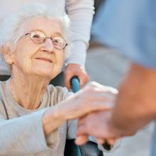 Frau im Rollstuhl gibt Pflegerin die  Hand